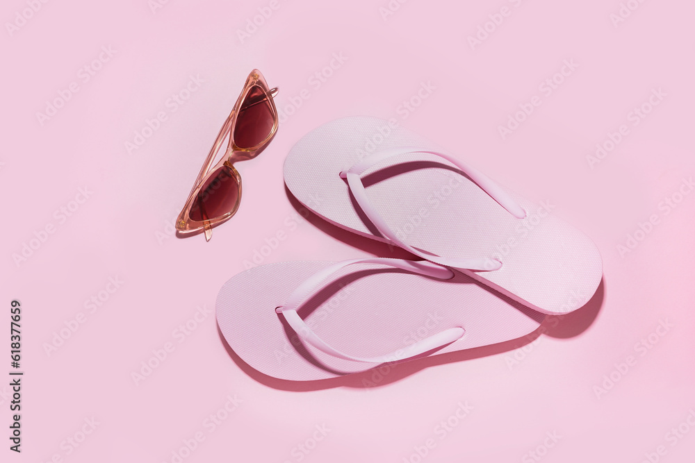 Pink flip-flops with sunglasses on color background