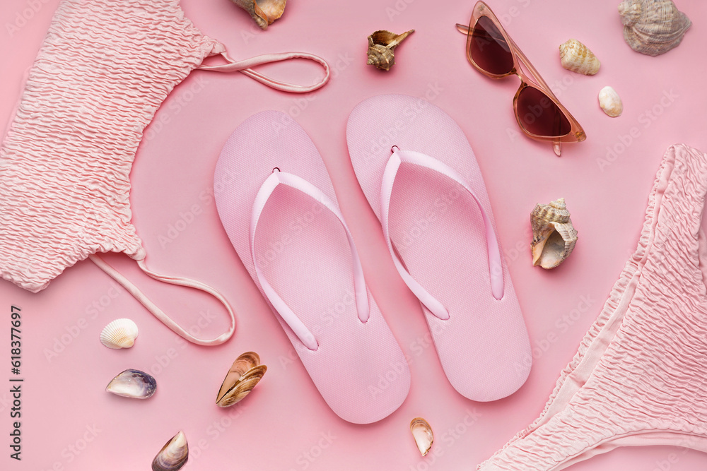 Pink flip-flops with swimsuit, sunglasses and shells on color background