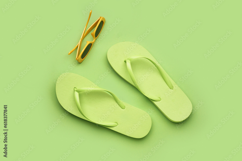 Green flip-flops with sunglasses on color background