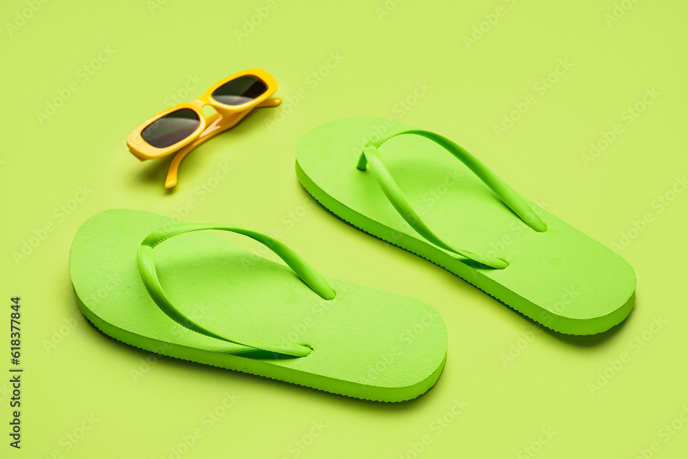 Green flip-flops with sunglasses on color background