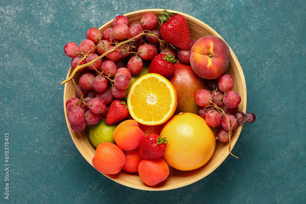 Bowl with different fresh fruits on blue background