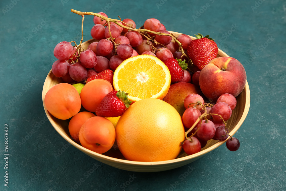 Bowl with different fresh fruits on blue background