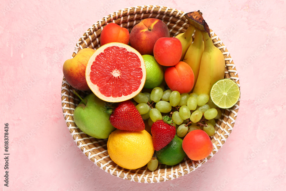 Wicker bowl with different fresh fruits on pink background