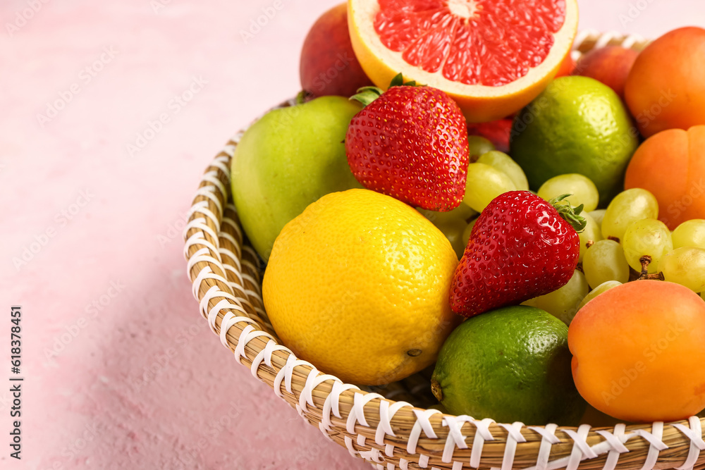 Wicker bowl with different fresh fruits on pink background