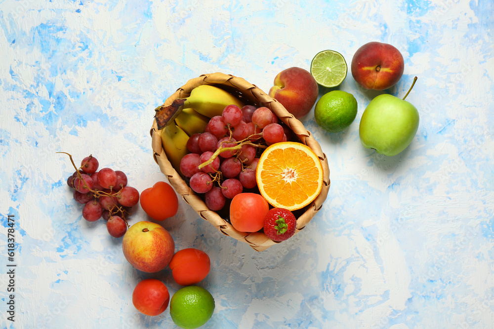 Wicker basket with different fresh fruits on light blue background