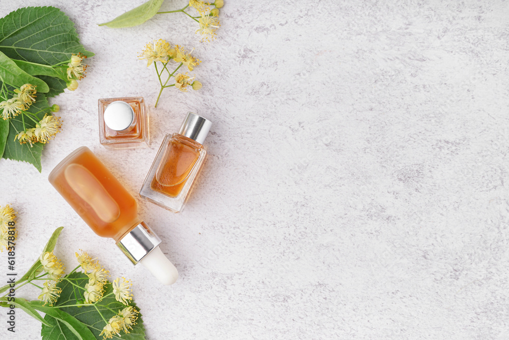 Bottles of essential oil and fresh linden flowers on light background