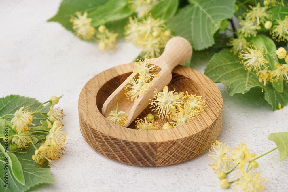 Composition with wooden plate, scoop, aromatic linden flowers and leaves on light background