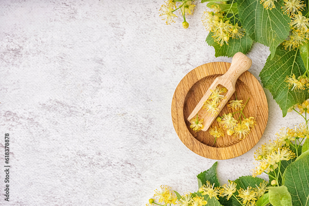 Composition with wooden plate, scoop, aromatic linden flowers and leaves on light background