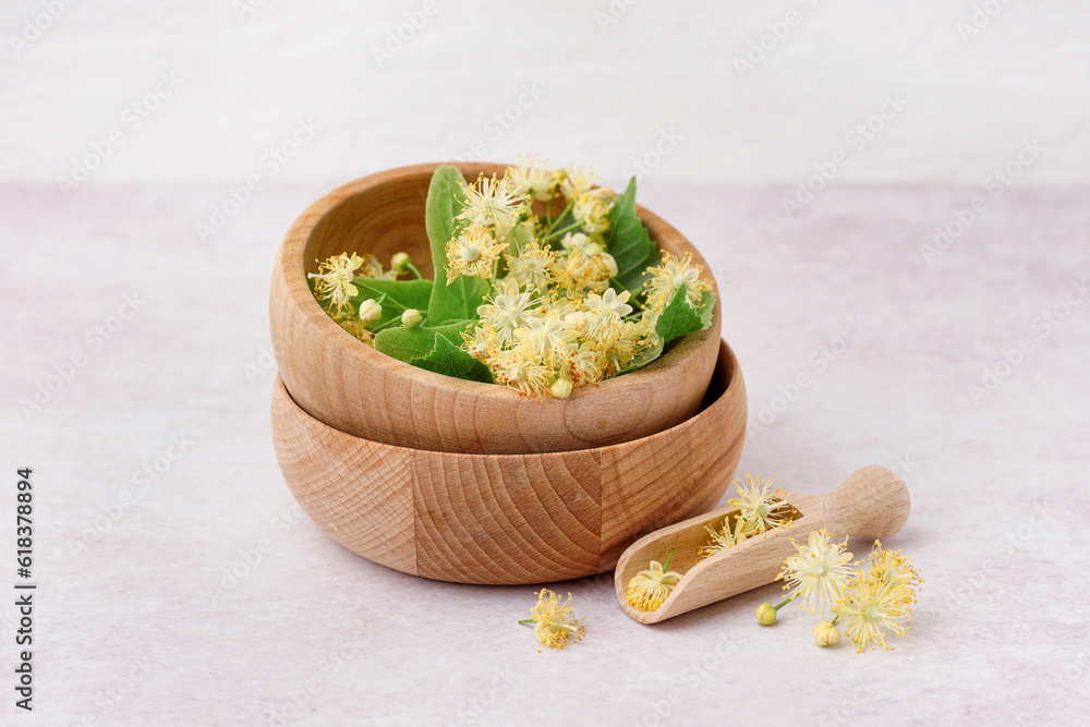 Wooden bowls with fresh linden flowers on light background