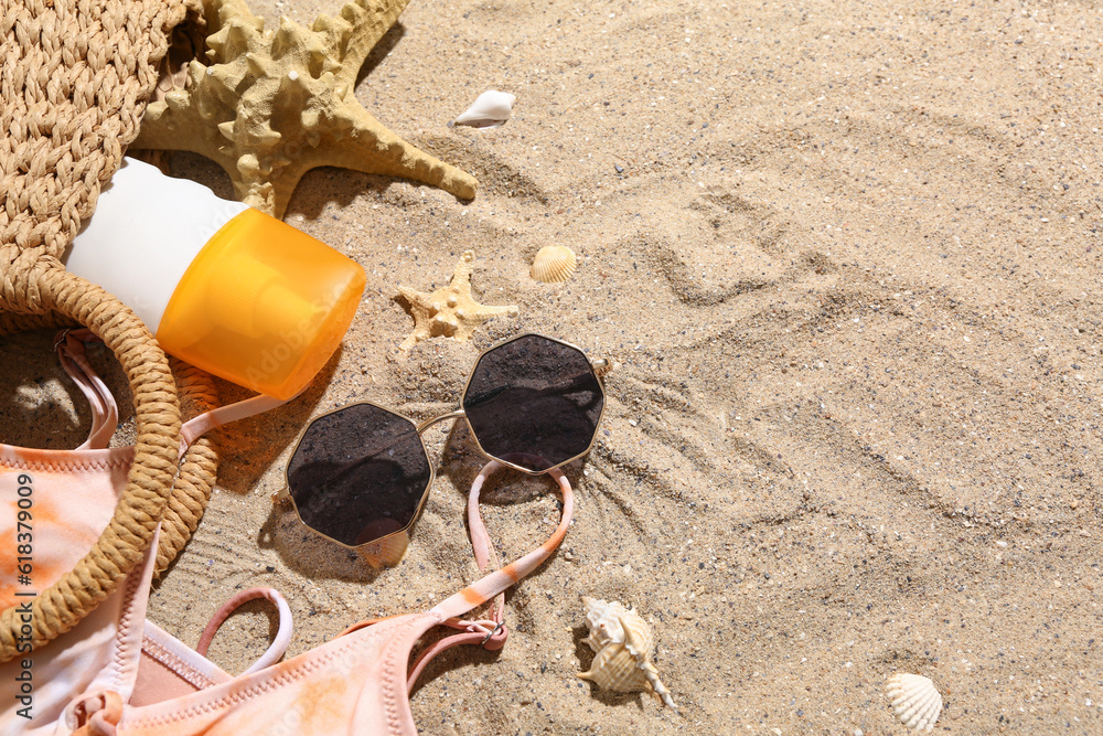 Wicker bag with sunglasses, bikini bra and bottle of sunscreen cream on sand