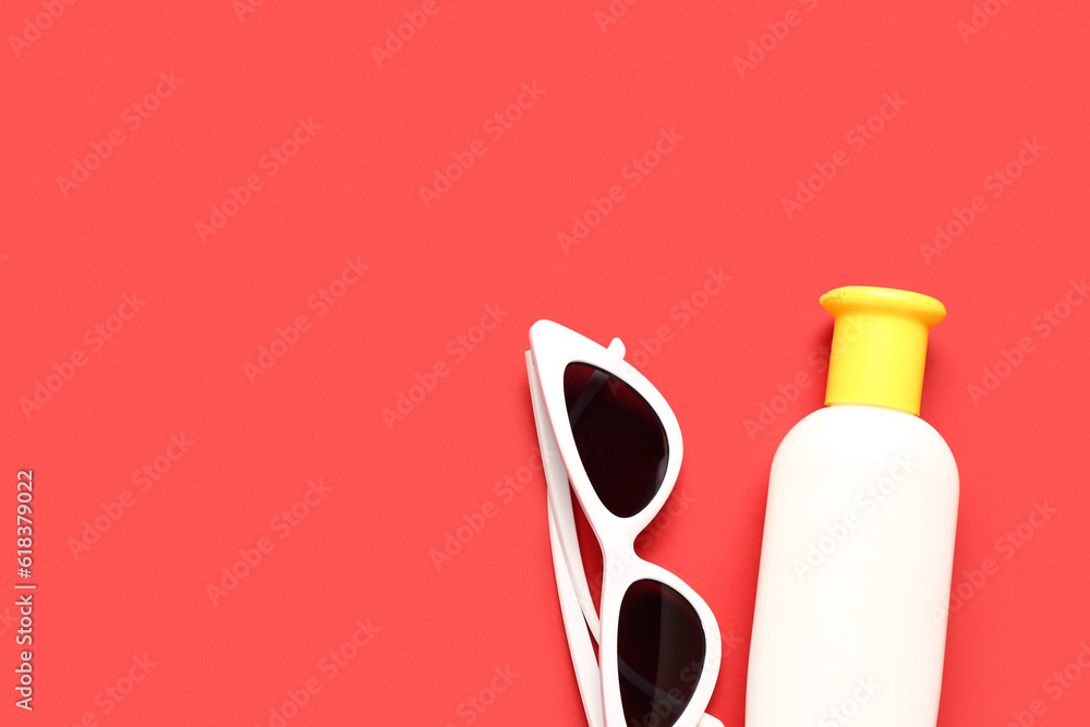 Sunglasses with bottle of sunscreen cream on red background