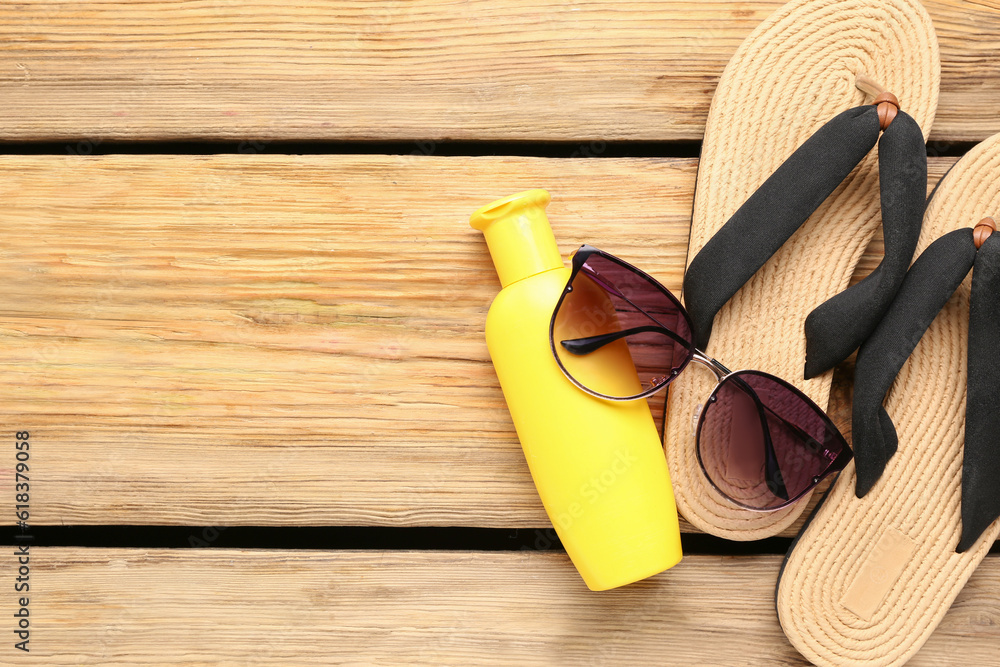 Sunglasses with flip flops, wicker hat and bottle of sunscreen cream on wooden background