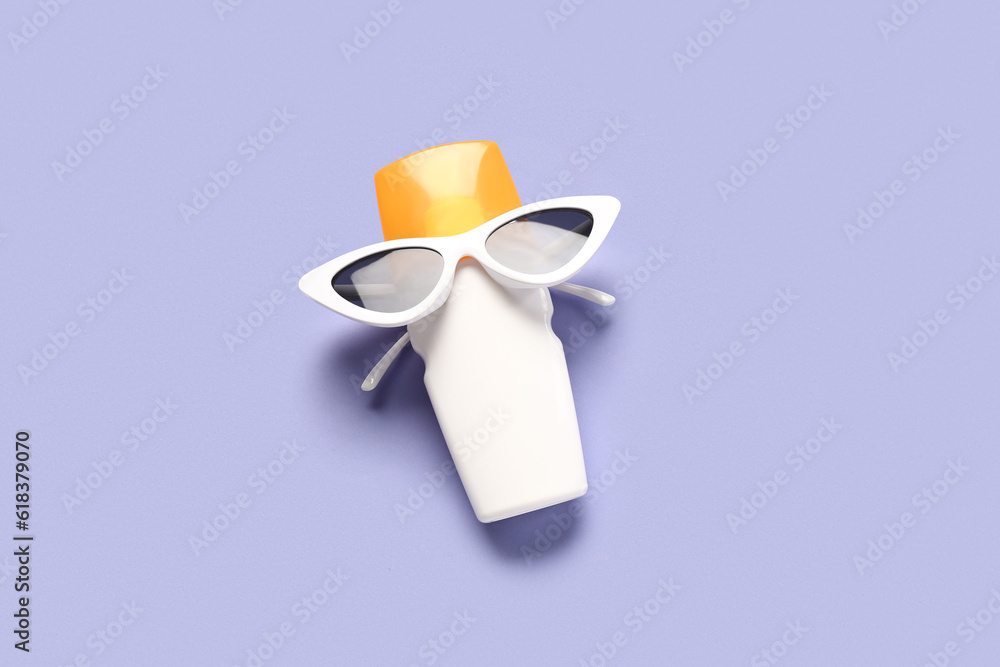 Creative composition with sunglasses and bottle of sunscreen cream on lilac background