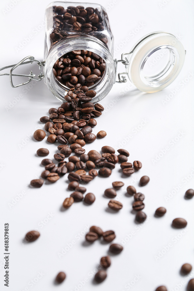 Glass jar with scattered coffee beans on white background