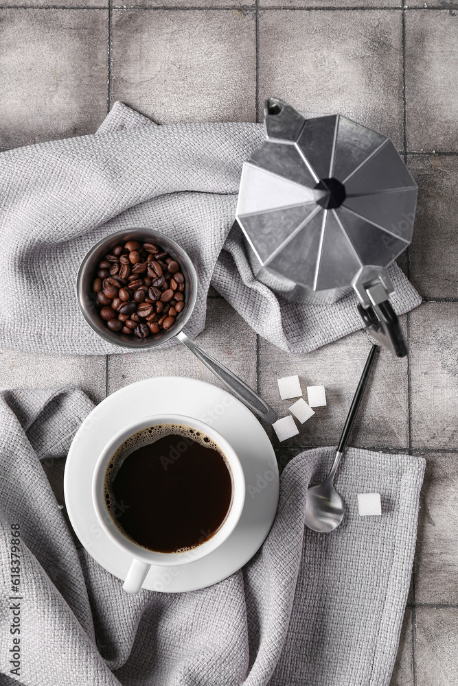 Coffee maker, cup and beans with fabric on tile background