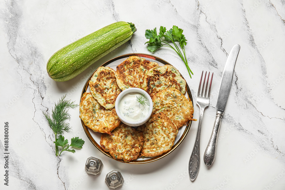 Plate of tasty zucchini fritters with sour cream on white marble background