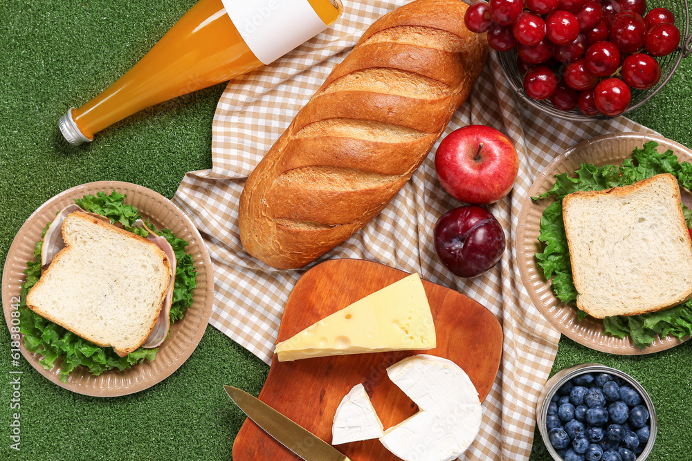 Composition with tasty sandwiches and different food for picnic on green background