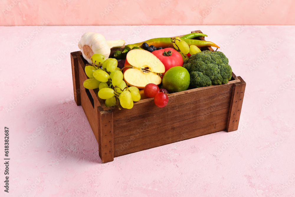 Wooden box with different fresh fruits and vegetables on pink background