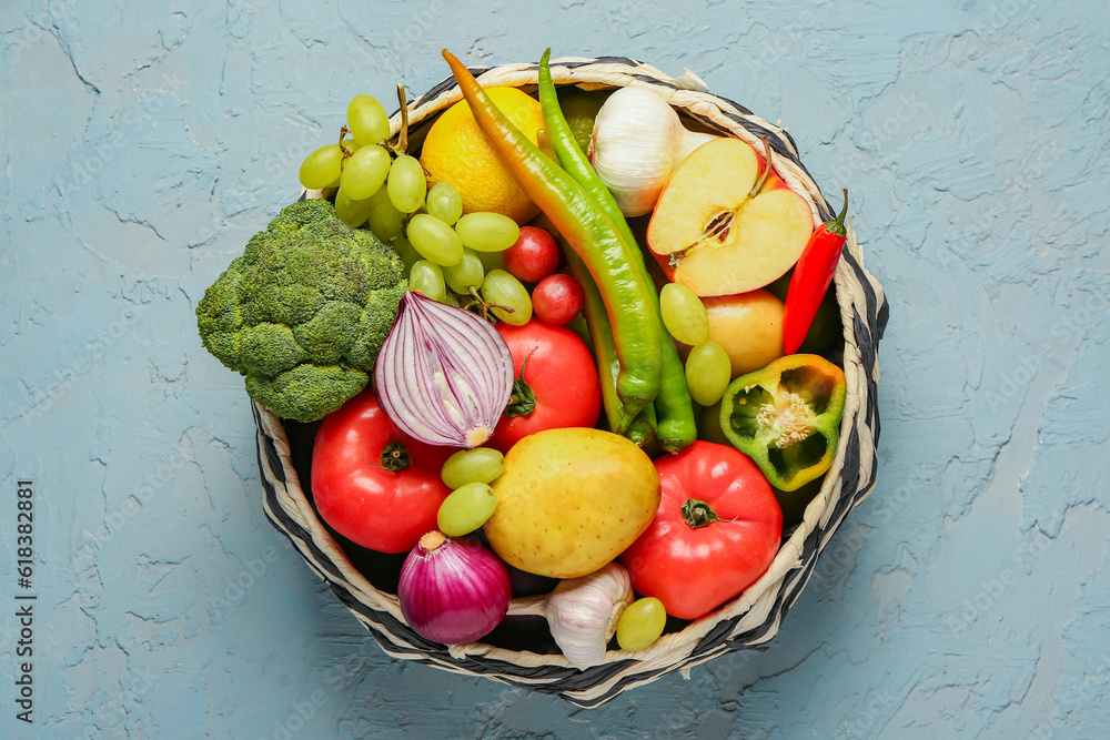 Wicker bowl with different fresh fruits and vegetables on blue background