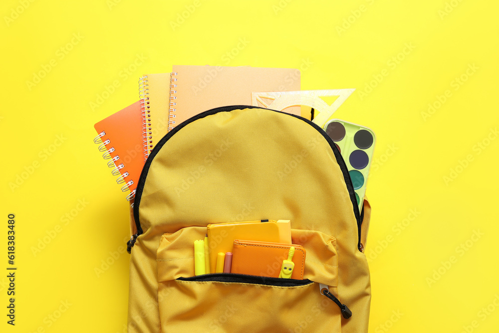 School backpack with notebooks, watercolors and markers on yellow background