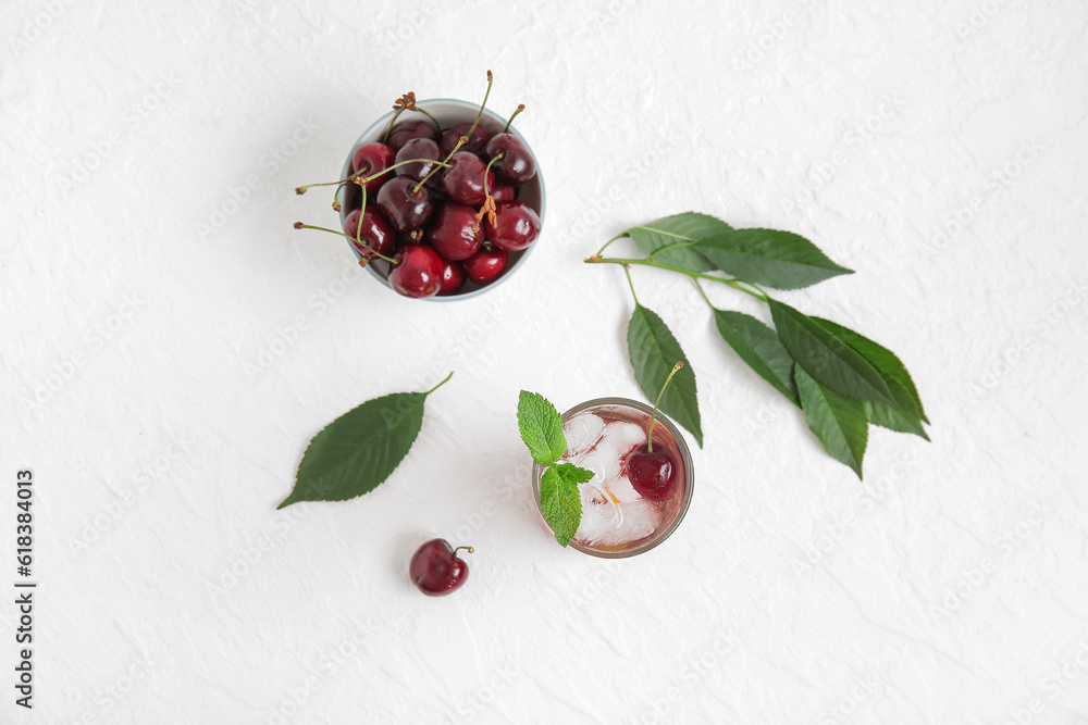 Glass of tasty cherry lemonade and bowl with berries on white background