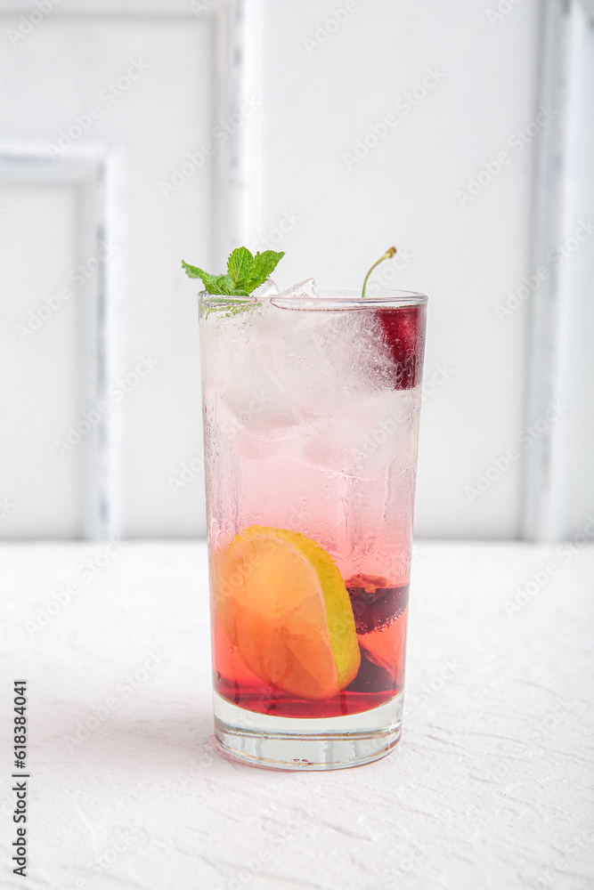 Glass of tasty cherry lemonade with lime and mint on white background