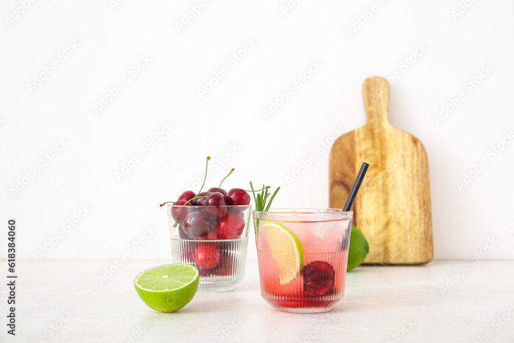 Glass of tasty cherry lemonade with lime and rosemary on white background