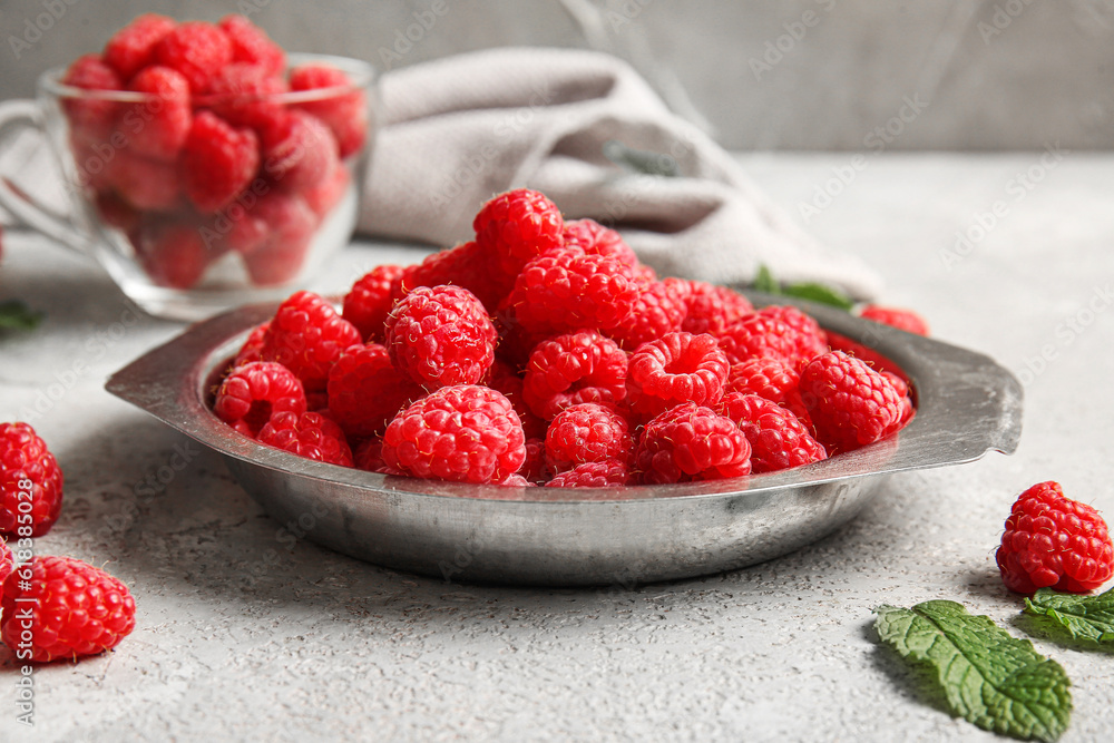 Metal plate and glass cup with fresh raspberries on grey background