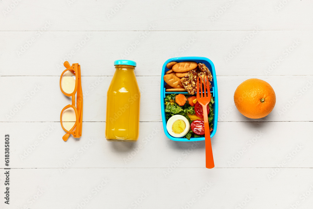 Bottle of juice, eyeglasses, orange and lunchbox with tasty food on white wooden background