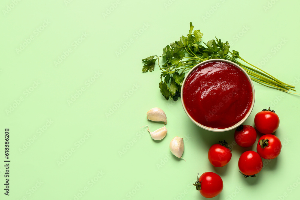 Bowl with tomato paste and fresh vegetables on green background