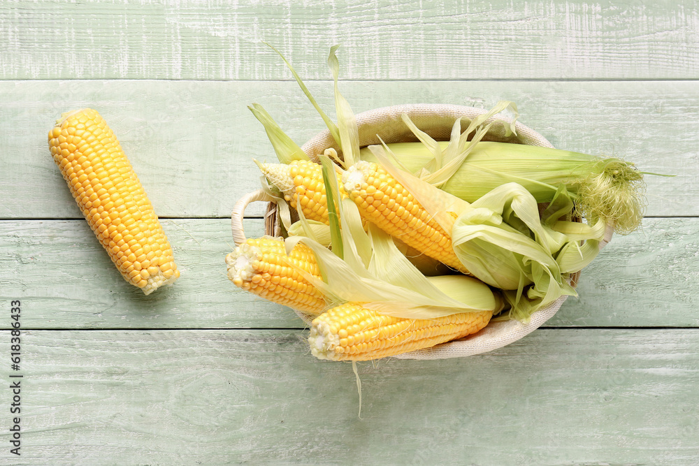 Wicker bowl with fresh corn cobs on green wooden background