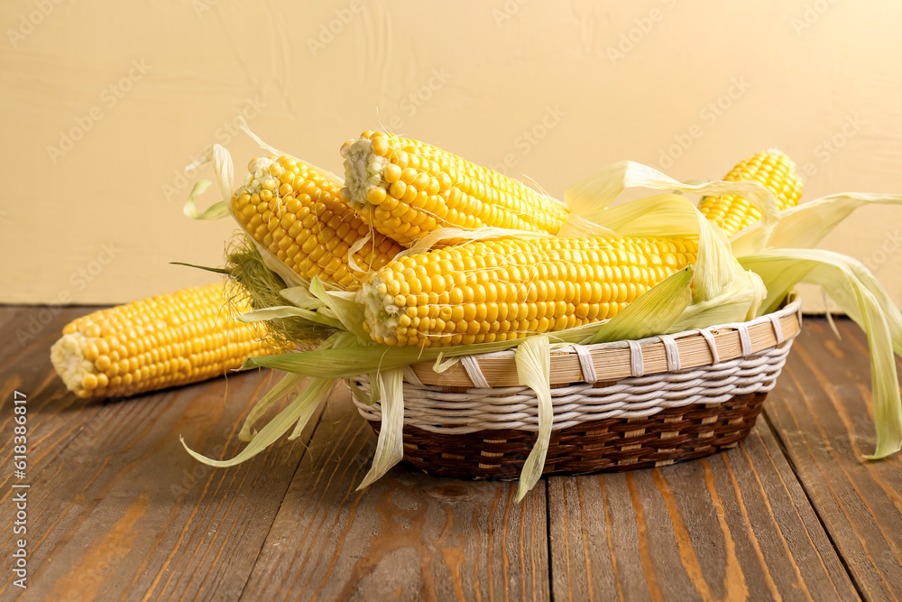 Wicker bowl with fresh corn cobs on wooden table