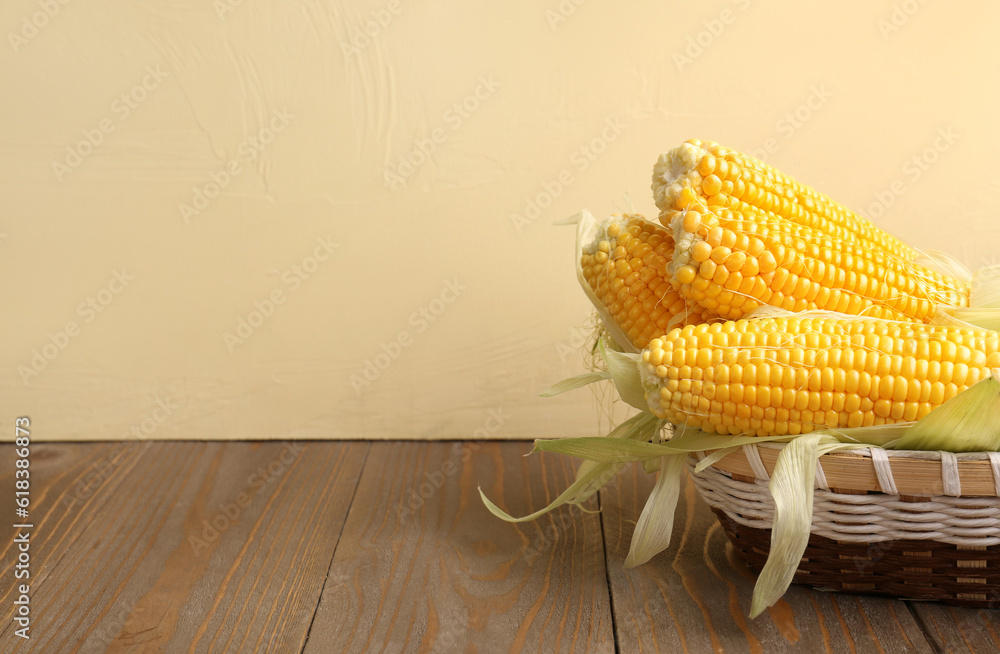 Wicker bowl with fresh corn cobs on wooden table