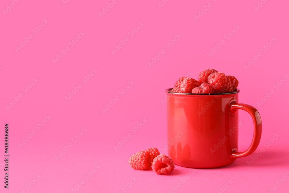 Cup with fresh raspberries on pink background