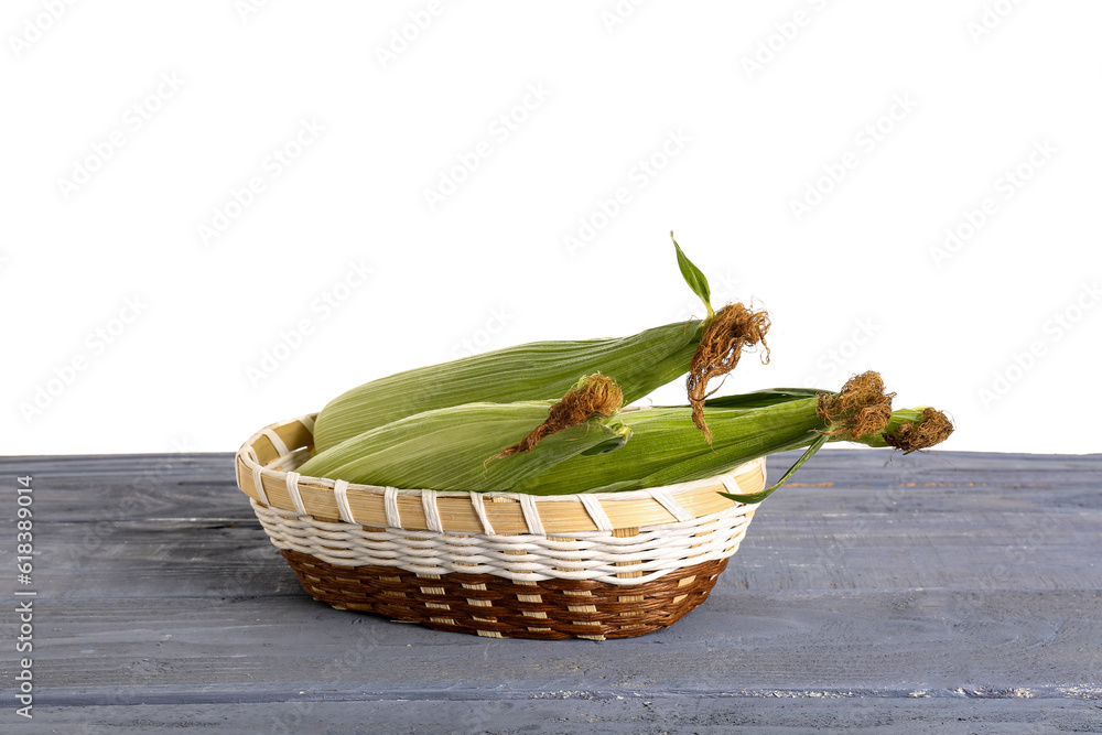 Wicker bowl with fresh corn cobs on blue wooden table against white background