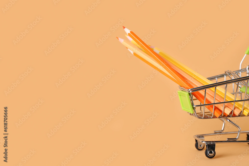 Shopping cart with pencils on color background