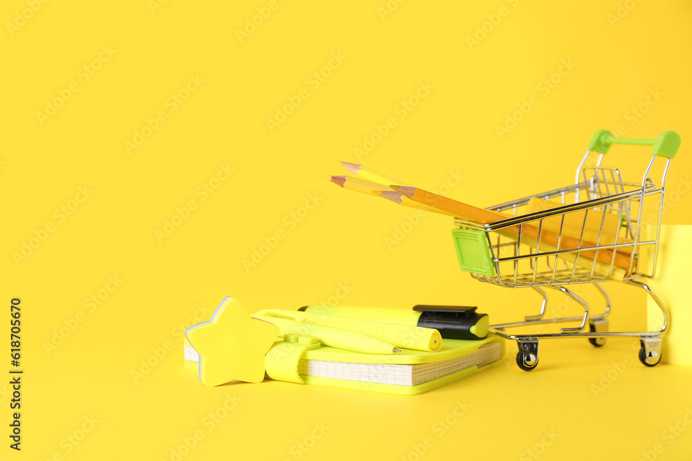 Set of different stationery and shopping cart on yellow background