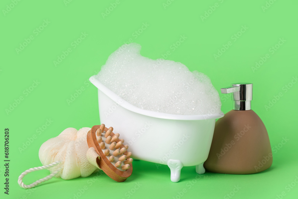 Small bathtub with foam and bath supplies on green background