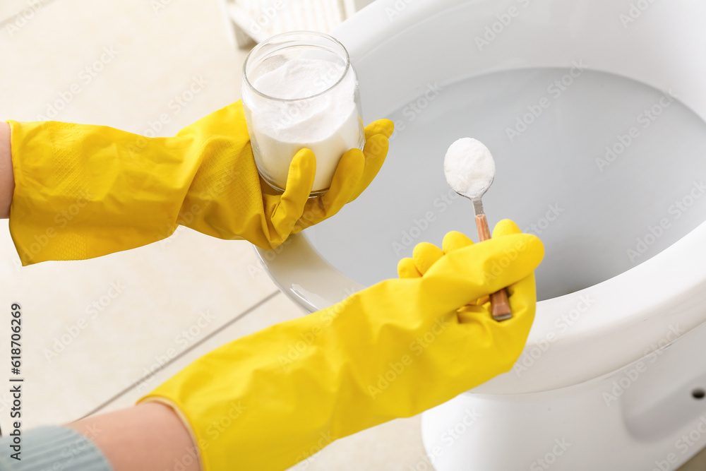 Woman in rubber gloves cleaning toilet bowl with baking soda, closeup