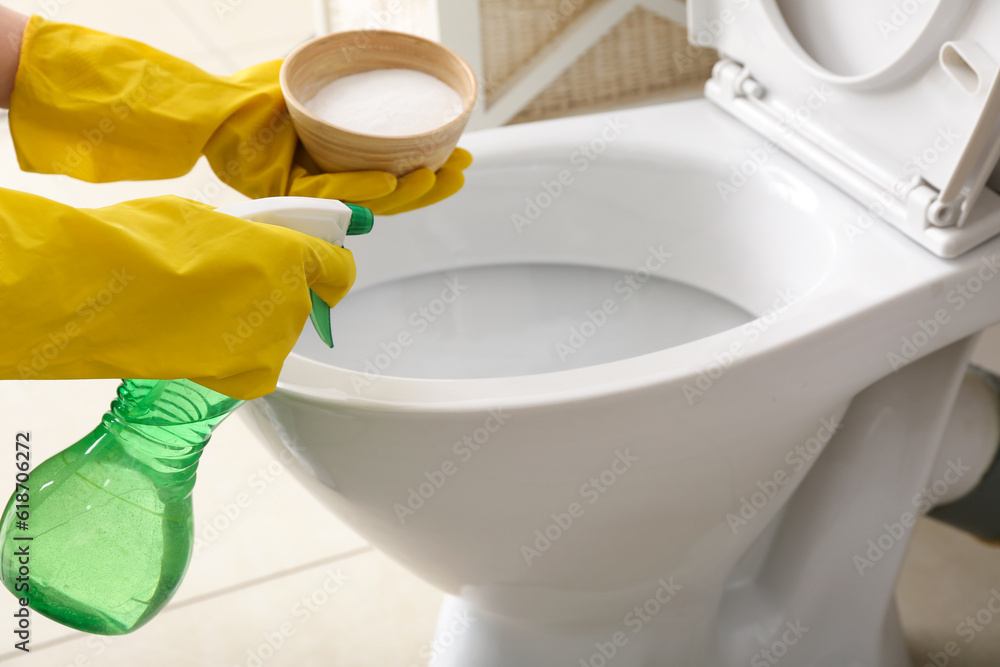 Woman in rubber gloves cleaning toilet bowl with baking soda and sprayer, closeup