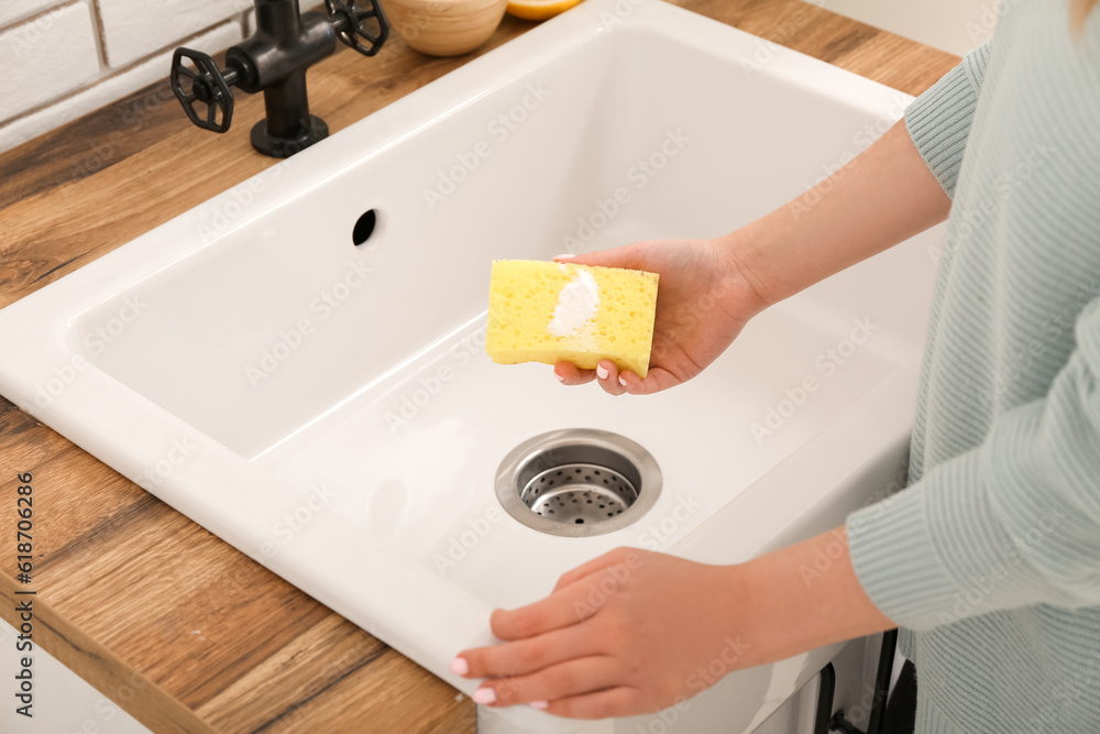 Woman cleaning white sink with sponge and baking soda, closeup