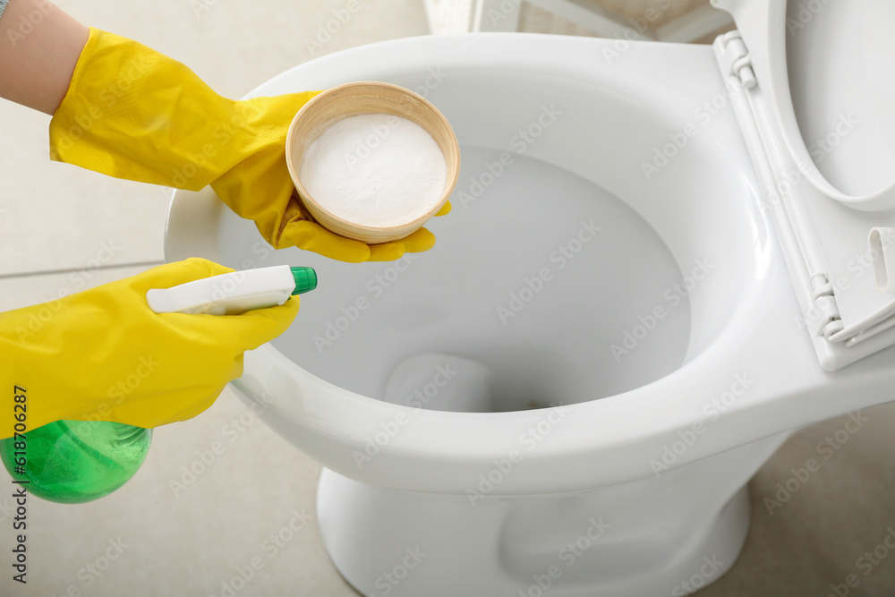 Woman in rubber gloves cleaning toilet bowl with baking soda and sprayer, closeup