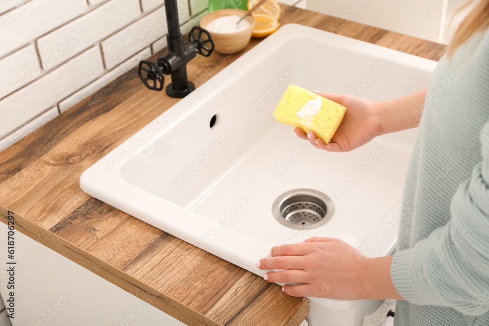 Woman cleaning white sink with sponge and baking soda