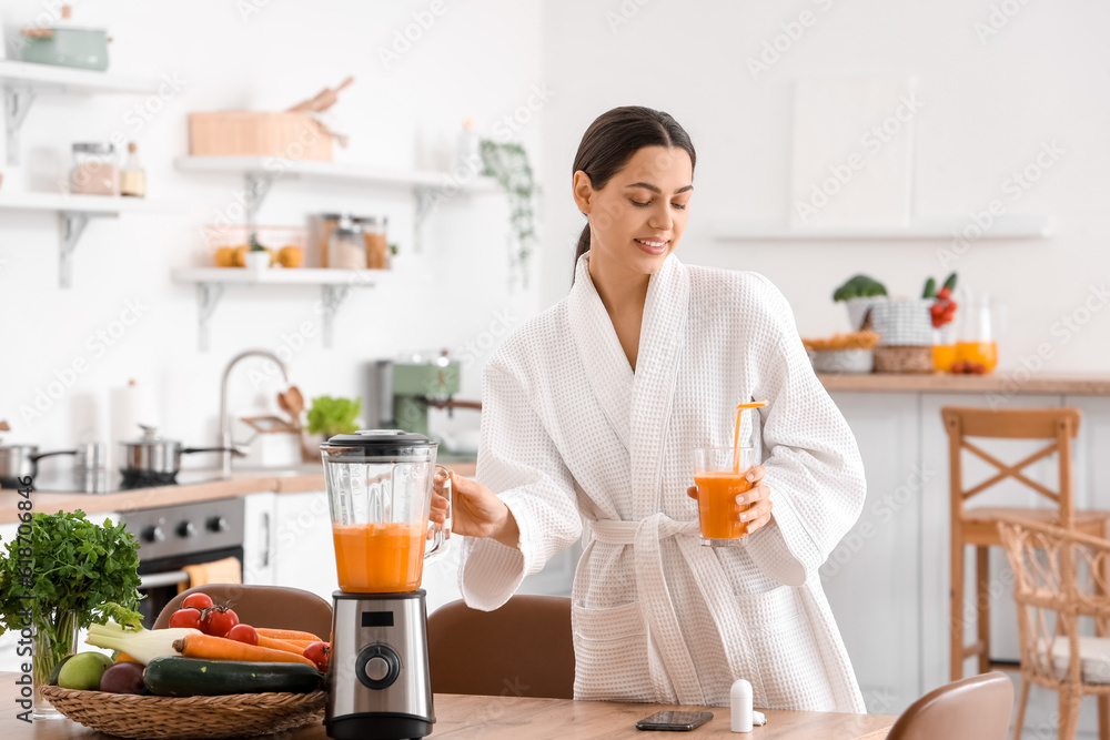 Young woman with glass of vegetable juice and blender in kitchen