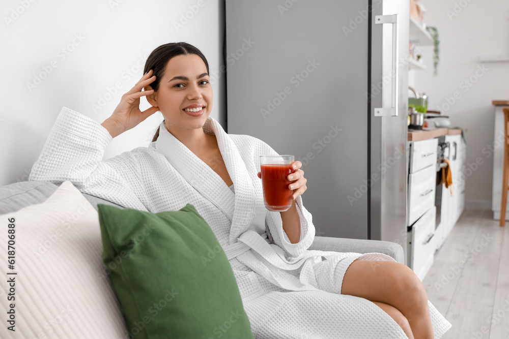 Young woman with glass of vegetable juice on sofa in kitchen