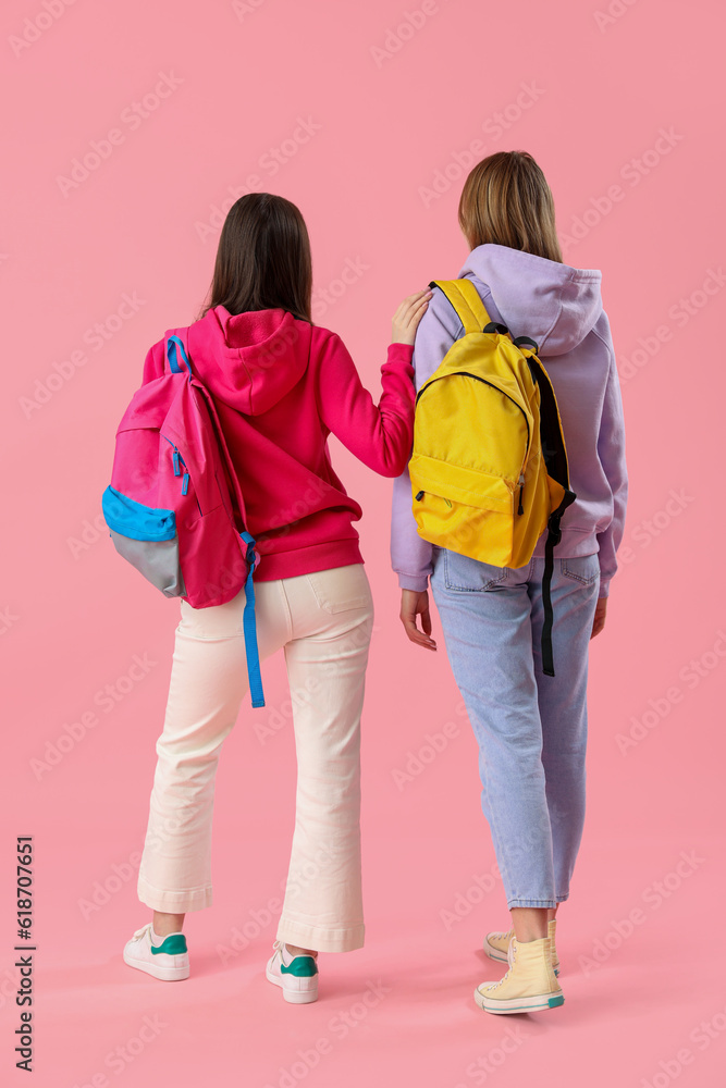 Female students with backpacks on pink background, back view