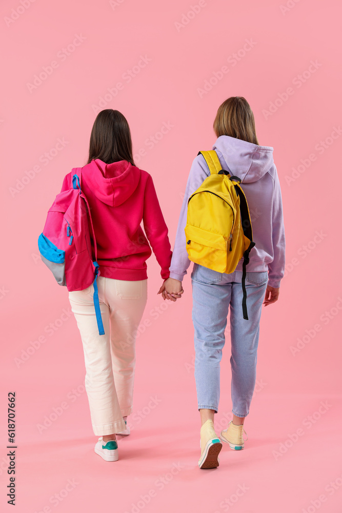 Female students with backpacks on pink background, back view