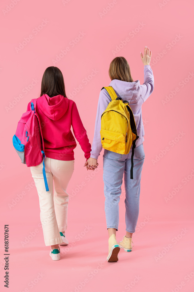 Female students with backpacks on pink background, back view