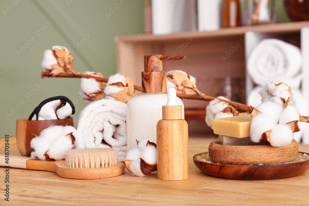 Set of cosmetic products, bath supplies and cotton branch on wooden table near color wall