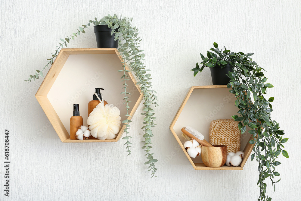 Wooden shelves with cosmetic products, bath supplies, cotton flowers and houseplants on on light wal